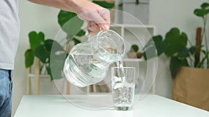 Man pours cold water into glass. Close-up of male hands pouring water from a jug into glass tumbler.