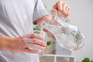 Man pours cold water into glass. Close-up of male hands pouring water from a jug into glass tumbler.