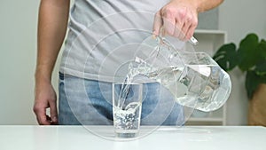 Man pours cold water into glass. Close-up of male hands pouring water from a jug into glass tumbler.