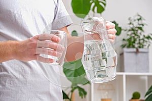 Man pours cold water into glass. Close-up of male hands pouring water from a jug into glass tumbler.