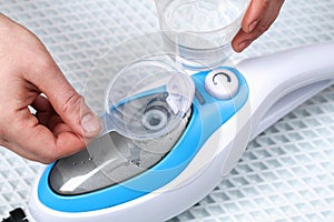 A man pours distilled water into container of a steam cleaner, steam mop.