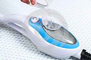 A man pours distilled water into container of a steam cleaner, steam mop.