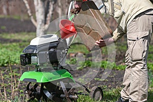 A man pours gasoline from the canister into the cultivator tank