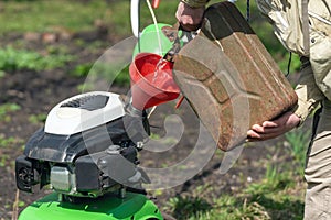 A man pours gasoline from the canister into the cultivator tank