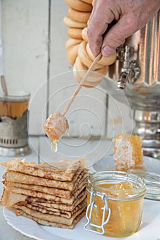 A man pours honey on pancakes and drinks tea from a samovar, Russian tradition of celebrating Maslenitsa
