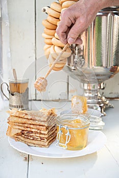 A man pours honey on pancakes and drinks tea from a samovar, Russian tradition of celebrating Maslenitsa