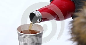 A man pours hot tea from a thermos in winter against the background of snow