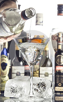 A man pours a martini from a bottle into a glass. On the table lies a large piece of ice.