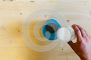 A man pours milk from a glass into a blue shaker to stir the protein. Whey protein, a healthy lifestyle, the person pouring a powd