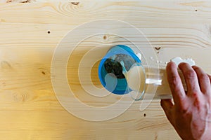 A man pours milk from a glass into a blue shaker to stir the protein. Whey protein, a healthy lifestyle, the person pouring a powd