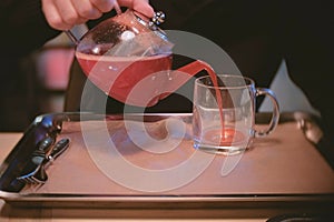 Man pours some cranberry tea from teapot to cup. Close-up man`s hands.