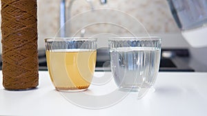 A man pours water from a teapot into a glass and puts a pure water filter, near a dirty water filter and a glass of