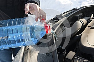 A man pours winter windscreen-washing liquid into the car outdoors
