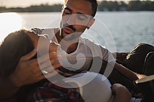 Man pouting while holding his smiling girlfriend by the river