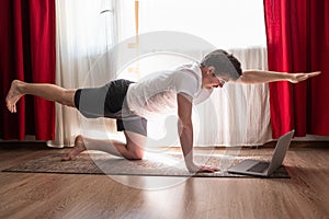 Man practices yoga asana chakravakasana or bird pose at the living room