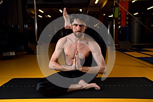 Man practices yoga in a dark gym. He threw his leg behind his head. Shirshasana