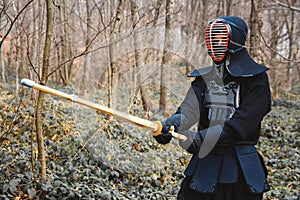 Man practicing kendo with shinai bamboo sword on forest background. Place for text or advertising