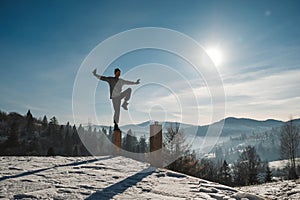 Man practicing yoga and balancing exercises in the winter mountains and enjoying life. Copy, empty space for text