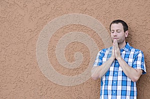 Man praying with a beige stucco wall as the background.