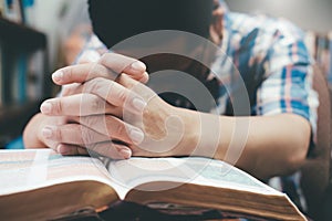 Man praying, hands clasped together on her Bible.