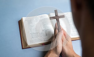 Man praying holding cross crucifx with open bible at the background