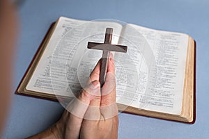 Man praying holding cross crucifx with open bible at the background
