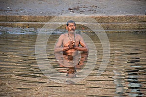 Man praying inside the holy waters of river Ganga in Varanasi, India
