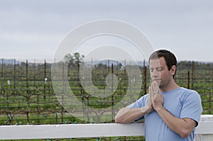 Man praying leaning on a white fence in a vineyard.