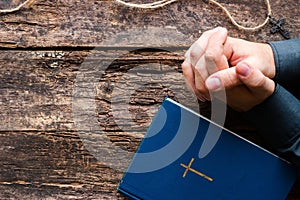 Man praying next to the bible and cross on a wooden background with space for text