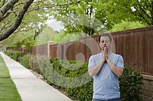 Man praying outside along a pathway.