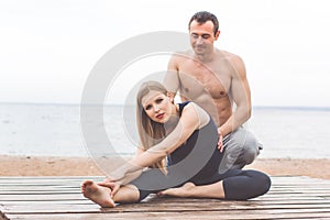 Man and pregnant girl are doing yoga at sea coast
