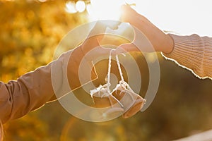 Man and pregnant wife are doing heart gesture with hands and holding warm baby shoes on nature autumn background