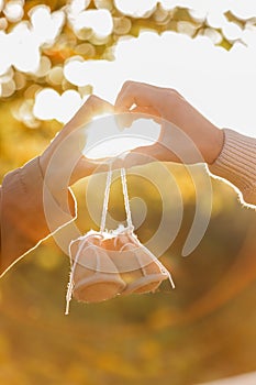 Man and pregnant wife are doing heart gesture with hands and holding warm baby shoes on nature autumn background