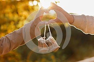 Man and pregnant wife are doing heart gesture with hands and holding warm baby shoes on nature autumn background