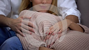 Man and pregnant wife hugging, male hand lying on female belly, happiness