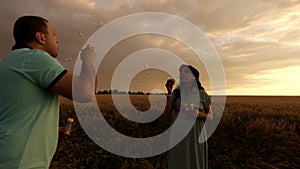 A man and a pregnant woman are blowing up soap bubbles standing in a wheat field in slowmo