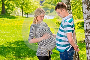 Man and pregnant woman compare their stomachs, shot in the park