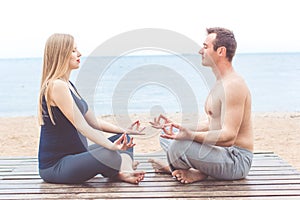 Man and pregnant woman are doing yoga on the beach