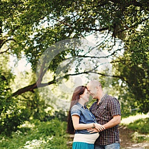 Man and pregnant woman, embracing in park outdoors