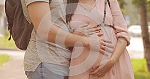 Man and pregnant woman in park touching and caressing belly hugging each other.