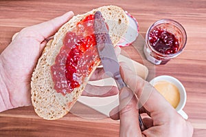 Man is prepairing breakfast and spreading jam on slice of bread