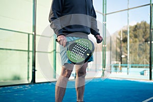 A man prepares for a backhand shot in padel tennis, with a focused expression and the court& x27;s fence shadow patterned