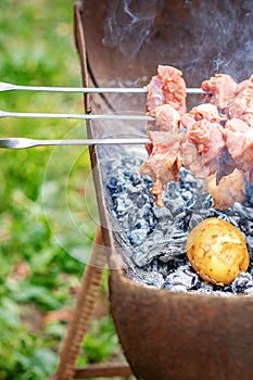 Man prepares barbecue meat with potatoes