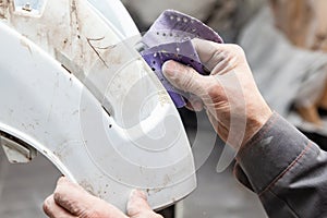 A man prepares a car body element for painting after an accident with the help of abrasive paper in a car repair shop. Recovery