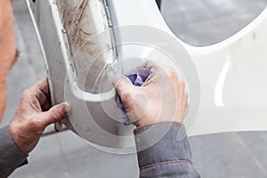 A man prepares a car body element for painting after an accident with the help of abrasive paper in a car repair shop. Recovery