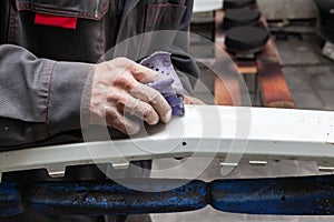 A man prepares a car body element for painting after an accident with the help of abrasive paper in a car repair shop. Recovery