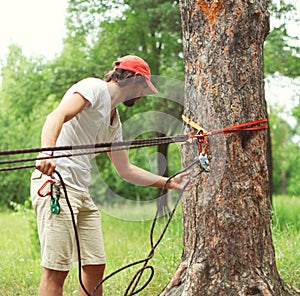 Man prepares a equipment fixes the carabiner on the rope tying for mountain climbing or slacklining in the park