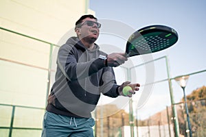 A man prepares to serve in a paddle tennis game, gripping the racket and ball, poised and ready for action