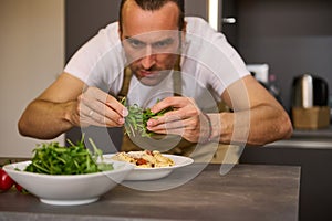 A man preparing dinner in home kitchen. Selective focus on hands holding greens for seasoning food. Male chef adding