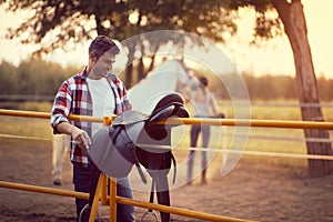 Man preparing a horse saddle for a ride. Training  on countryside, sunset golden hour. Freedom nature concept